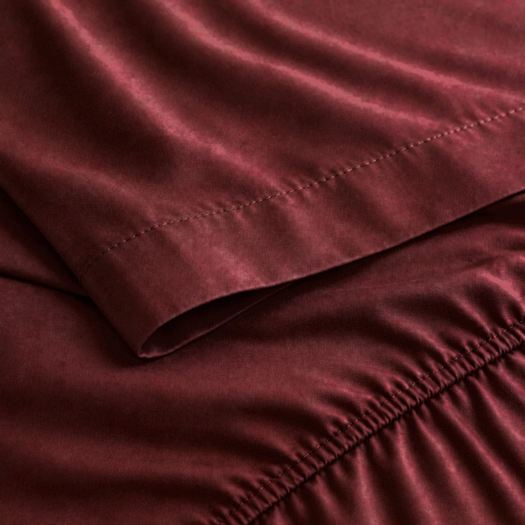 ruby red bamboo viscose sateen close-up of the flat sheet hem stitching and fitted sheet elastic edge