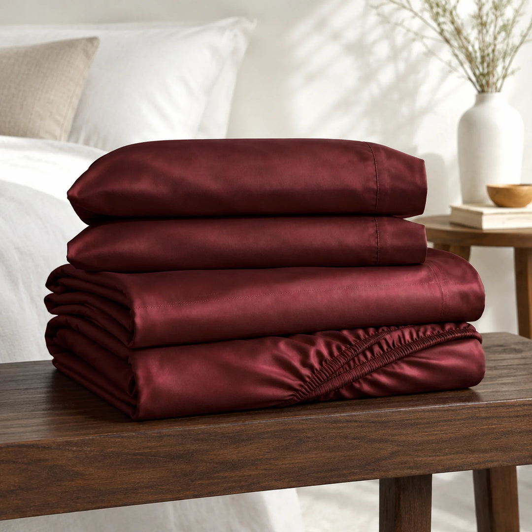 ruby red bamboo viscose sheet set folded on a walnut bench: flat sheet, fitted sheet and pillowcases