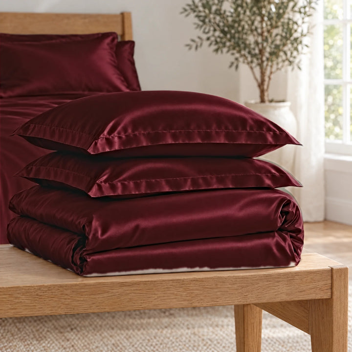 Ruby Red bamboo viscose Signature duvet cover and two shams, neatly folded in a stack on an oak bench
