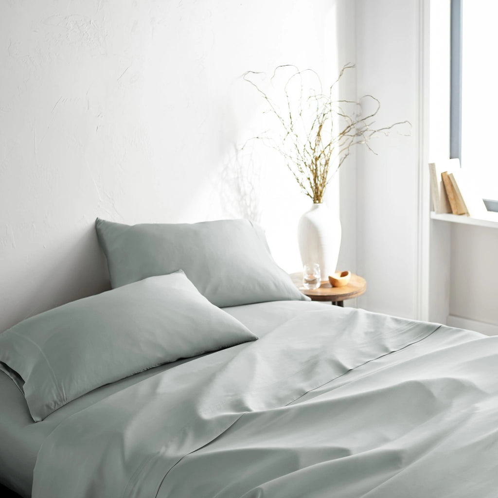 silver bamboo bed sheets with sateen weave from the Signature Collection, three-quarter angle showing natural folds and soft lighting from nearby window