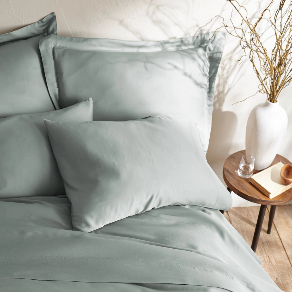 close-up of silver bamboo sateen pillowcases and duvet cover on king bed, styled against a textured cream wall with natural decor
