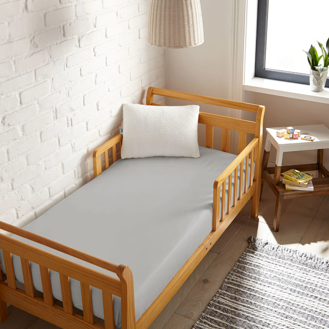 silver bamboo toddler fitted sheet from the Signature Collection, viewed from above on a light wood frame toddler bed in a bright modern nursery