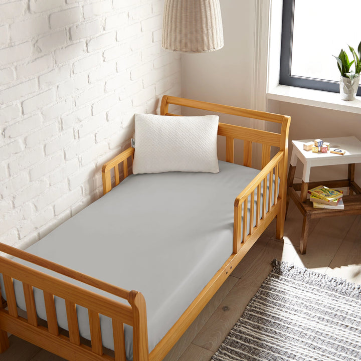 silver bamboo toddler fitted sheet from the Signature Collection, viewed from above on a light wood frame toddler bed in a bright modern nursery