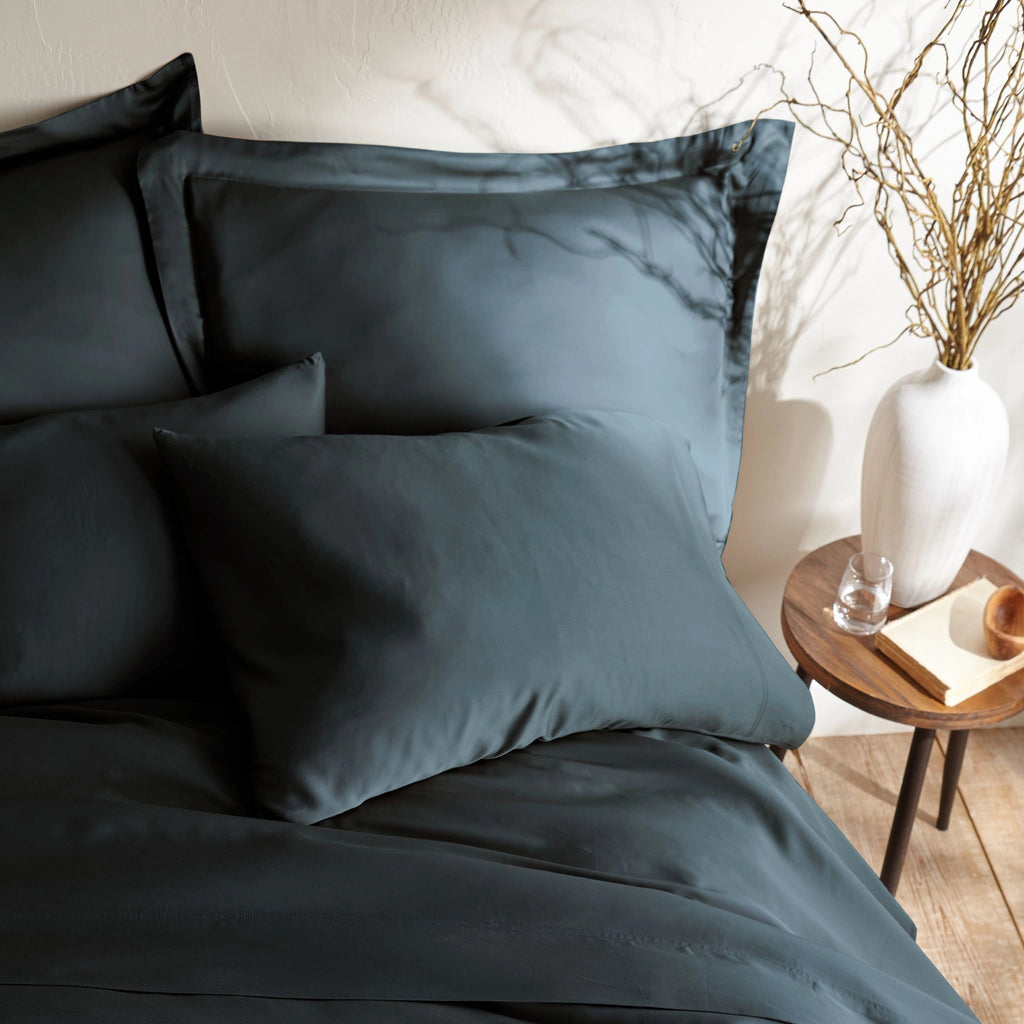 close-up of slate bamboo sateen pillowcases and duvet cover on king bed, styled against a textured cream wall with natural decor