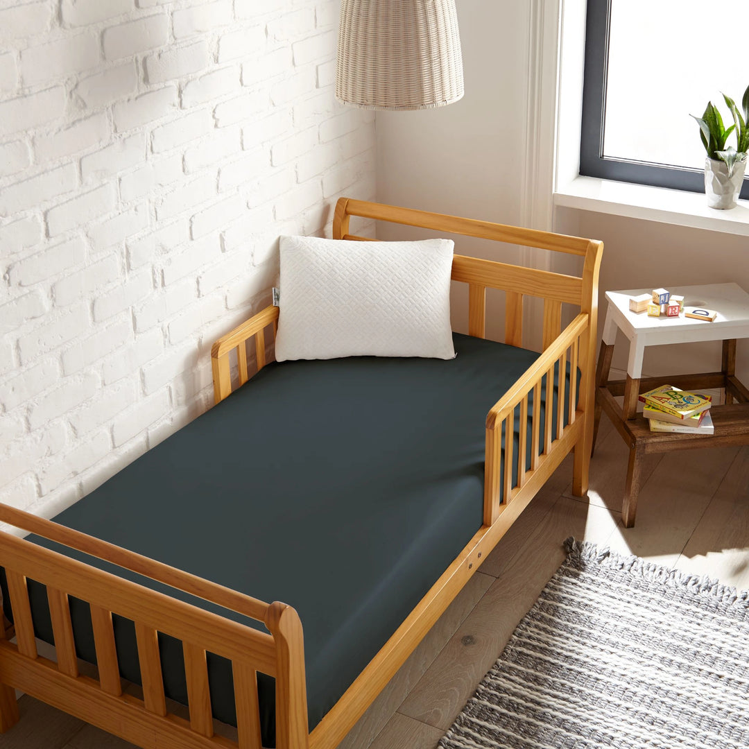slate bamboo toddler fitted sheet from the Signature Collection, viewed from above on a light wood frame toddler bed in a bright modern nursery