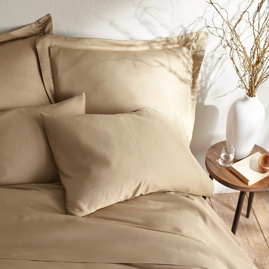 close-up of taupe bamboo sateen pillowcases and duvet cover on king bed, styled against a textured cream wall with natural decor