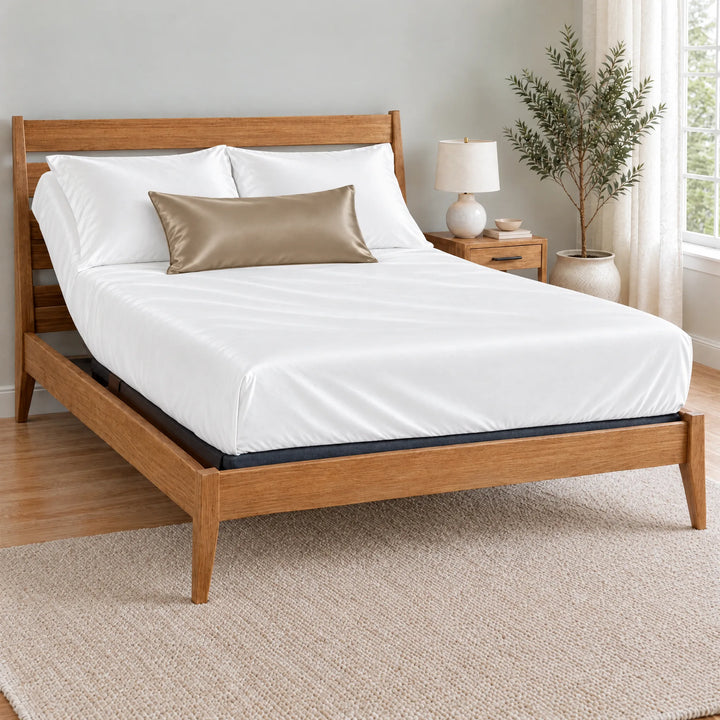 Taupe bamboo viscose sateen lumbar pillowcase on a made bed in front of white pillows in a light oak bedroom with an olive tree