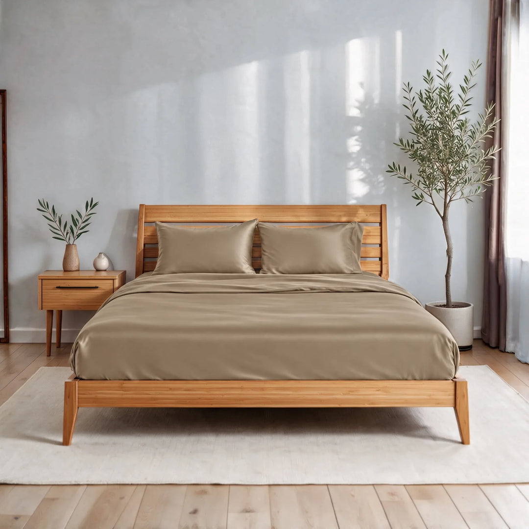 Taupe bamboo viscose sateen sheet set on a caramelized bamboo bed frame in a bright bedroom with a cream rug and olive tree
