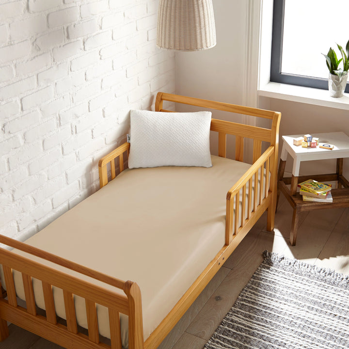 taupe bamboo toddler fitted sheet from the Signature Collection, viewed from above on a light wood frame toddler bed in a bright modern nursery