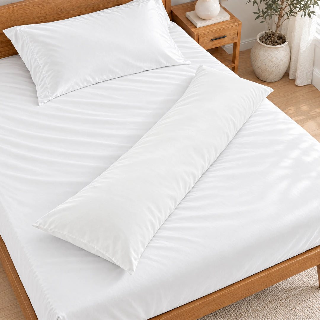 White bamboo viscose sateen body pillowcase lying diagonally across a made bed, overhead view in a bright bedroom with a honey bamboo bed
