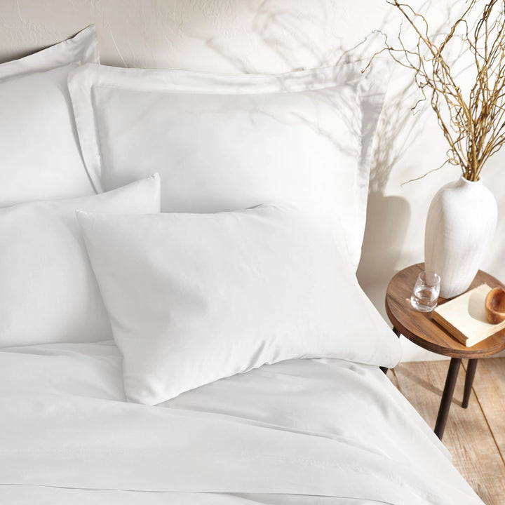 close-up of white bamboo sateen pillowcases and duvet cover on king bed, styled against a textured cream wall with natural decor