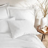 close-up of white bamboo sateen pillowcases and duvet cover on king bed, styled against a textured cream wall with natural decor