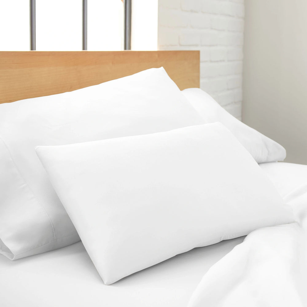 white bamboo lumbar pillowcase from the Signature Collection, shown upright against white pillows on a wood headboard in a minimalist bedroom