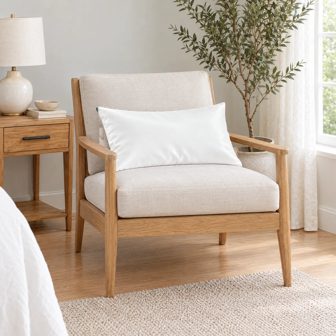 White bamboo viscose sateen lumbar pillowcase on a light oak armchair beside a nightstand and olive tree