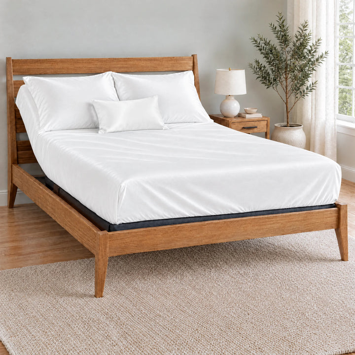 White bamboo viscose sateen lumbar pillowcase on a made bed in front of white pillows in a light oak bedroom with an olive tree