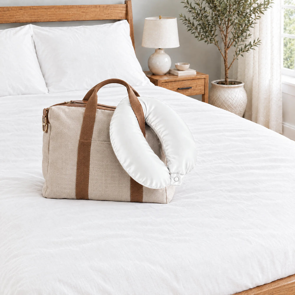 White bamboo viscose sateen neck pillowcase hanging from a linen tote handle on a made bed