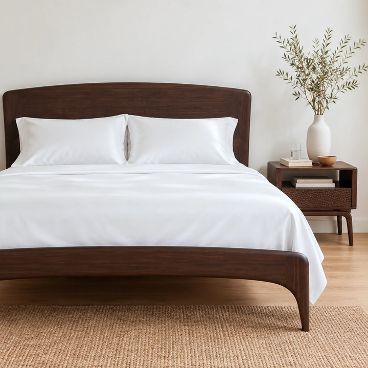 white bamboo viscose sateen sheet set on a dark walnut bed with a curved headboard in a bright bedroom