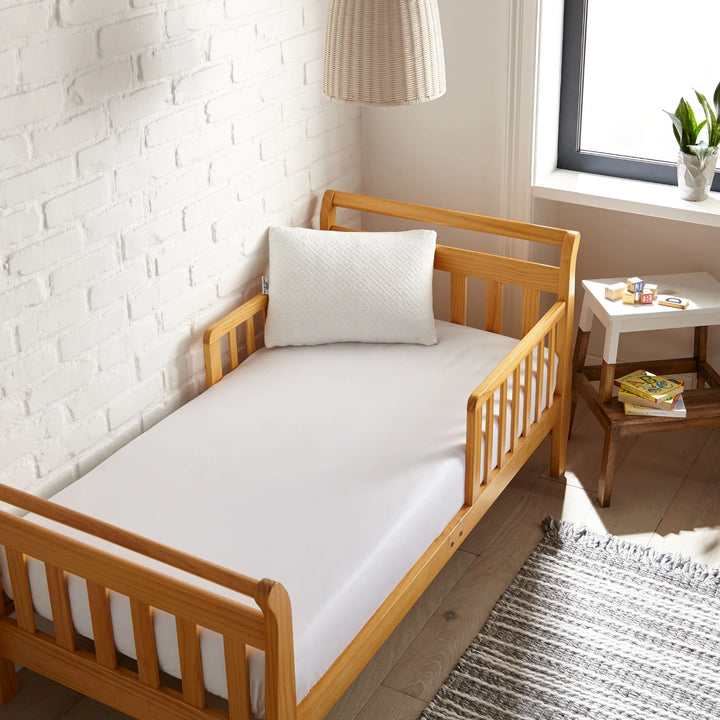 white bamboo toddler fitted sheet from the Signature Collection, viewed from above on a light wood frame toddler bed in a bright modern nursery