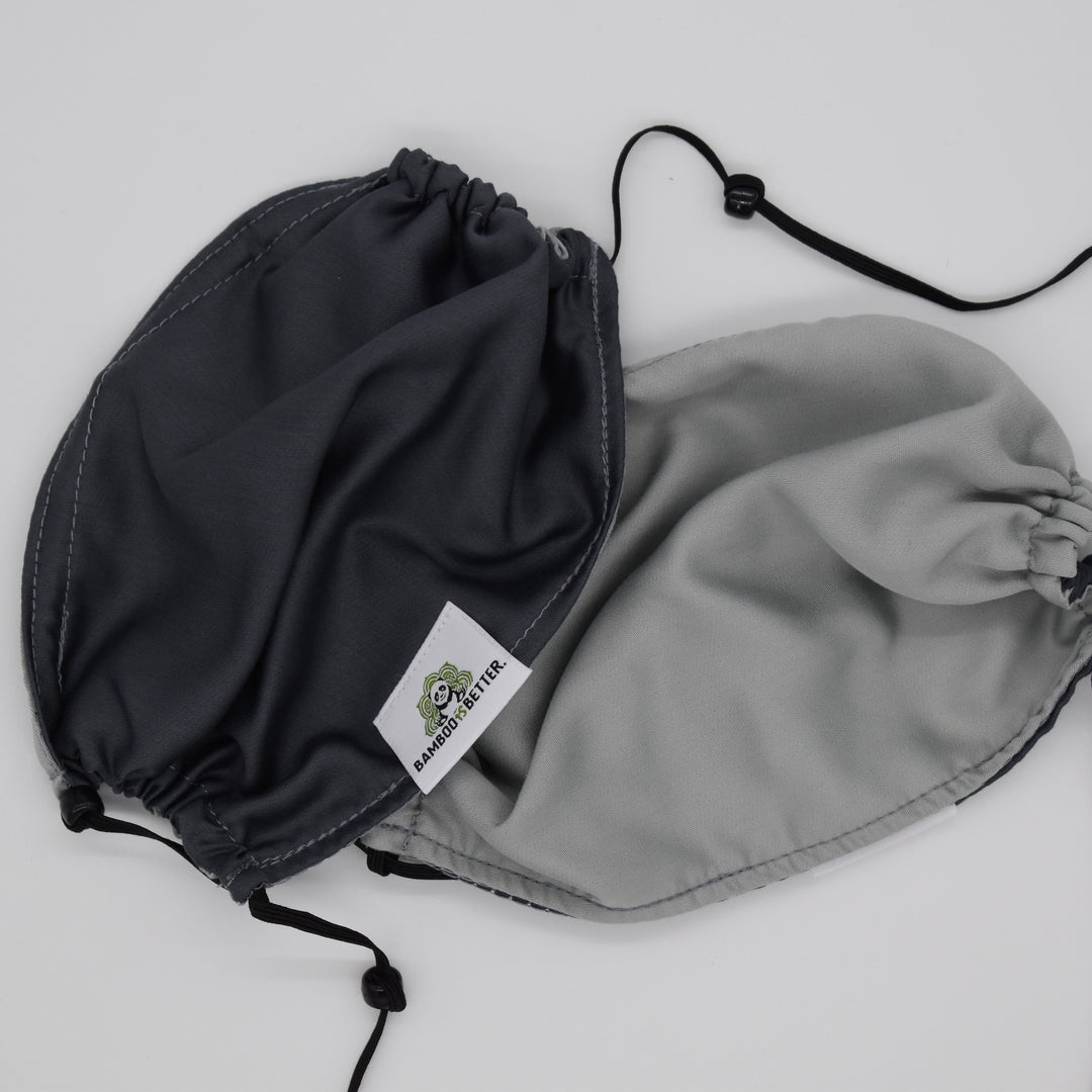 Reversible fabric face mask in dark gray and light gray, with adjustable ear loops and a brand label for a comfortable and secure fit.