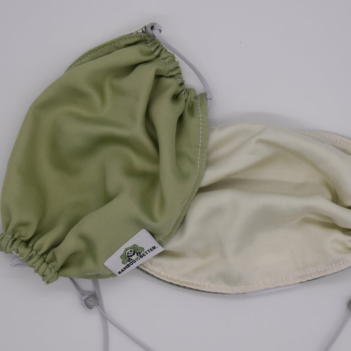 Reversible fabric face mask in green and cream, with adjustable ear loops and a brand label for a comfortable and secure fit.
