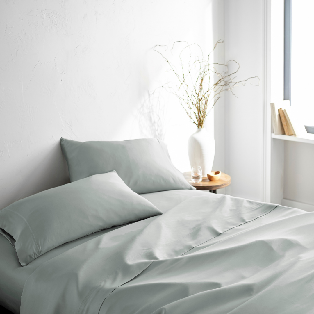 silver bamboo bed sheets with sateen weave from the Signature Collection, three-quarter angle showing natural folds and soft lighting from nearby window