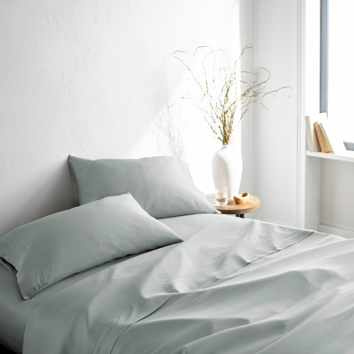 silver bamboo bed sheets with sateen weave from the Signature Collection, three-quarter angle showing natural folds and soft lighting from nearby window